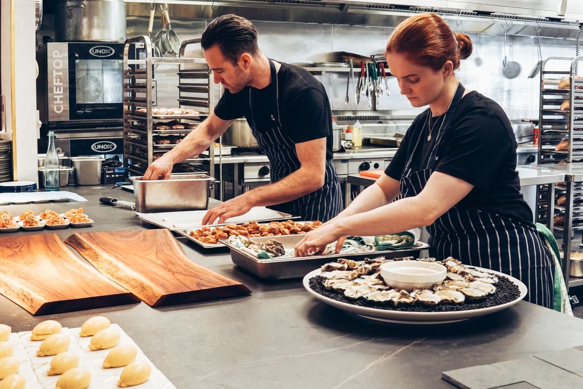 Two chefs plating appetisers on a stainless steel kitchen counter