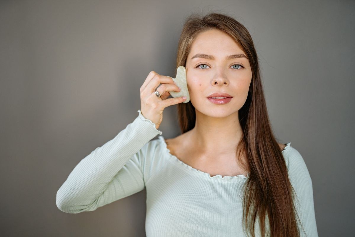 Woman pressing a heart-shaped jade gua sha tool along her cheek